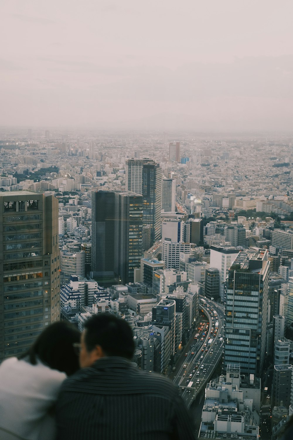 two people sitting on a ledge overlooking a city