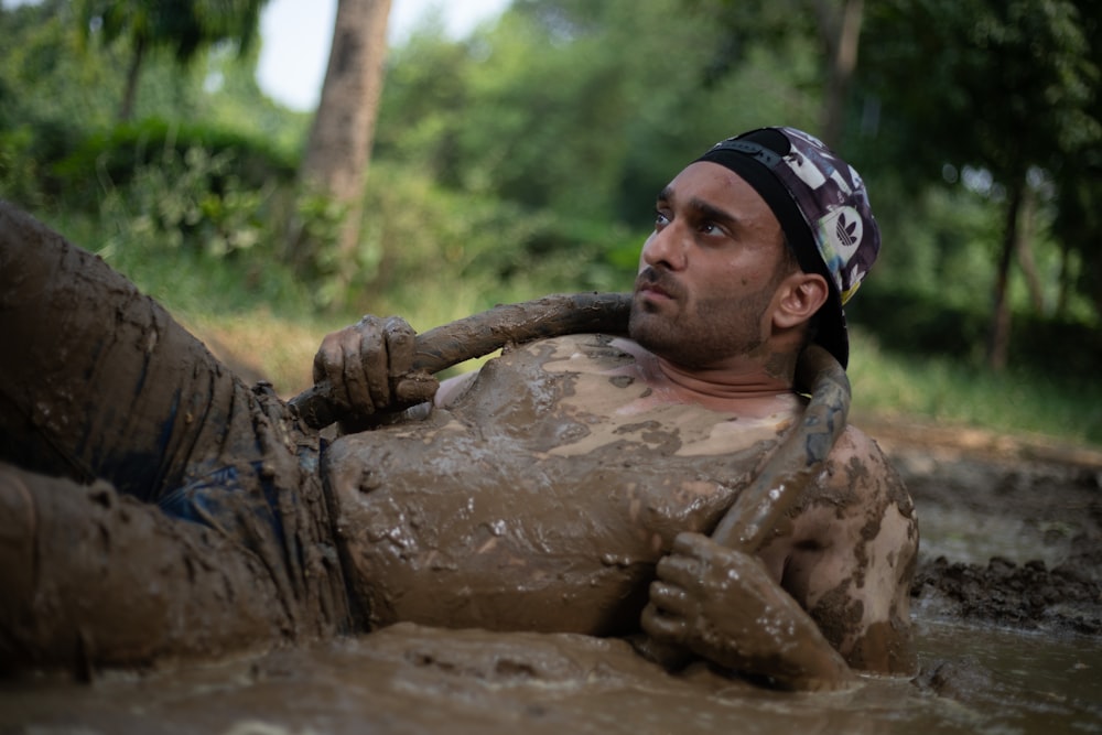 a man laying in the mud with a stick in his mouth