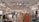 A clothing store interior featuring multiple racks with various garments. The ceiling has track lighting, and the walls are lined with shelves displaying folded clothes. Brick accents give an industrial feel, and the aisles are organized with apparel such as dresses, shirts, and jeans.
