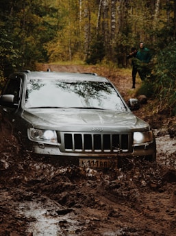 A rugged jeep driving through muddy off-road trails surrounded by tropical forest.