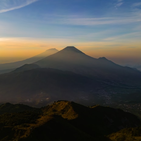 A panoramic view of a mountain ridge with layered peaks fading into the distance at sunset.