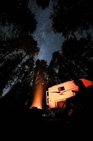 A starry night sky over a remote campsite with a campfire glowing softly in the foreground.