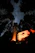 A close-up of a joyful traveler standing beside a roaring campfire under a starry jungle sky.