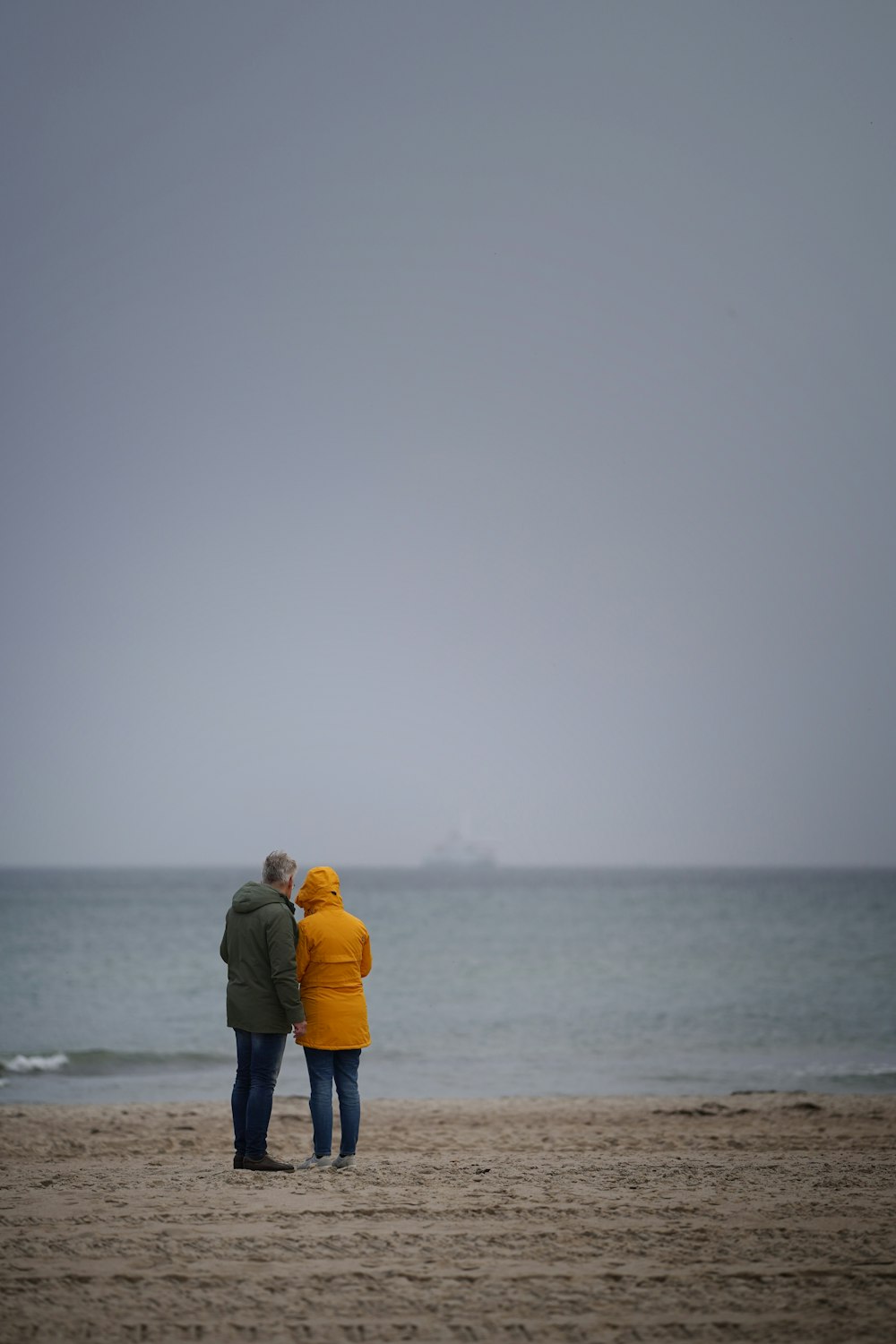 a couple of people standing on top of a sandy beach