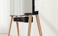 A modern television set up on sleek, angled wooden legs with a soundbar positioned directly beneath it. The design is minimalist and stylish, integrating functionality with aesthetics in a clean, contemporary space.