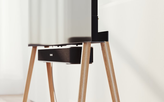 A modern television set up on sleek, angled wooden legs with a soundbar positioned directly beneath it. The design is minimalist and stylish, integrating functionality with aesthetics in a clean, contemporary space.