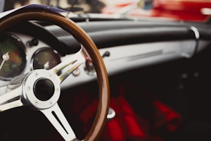 A close-up of a classic car interior highlighting a wooden steering wheel and the dashboard with vintage-style gauges. The tone of the image conveys a sense of nostalgia and sophistication with its retro aesthetic.
