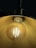 A close-up view of an illuminated incandescent light bulb housed within a brass or gold-colored metallic lamp shade. The bulb's glowing filaments are visible, casting a warm, ambient reflection on the inner surface of the shade.