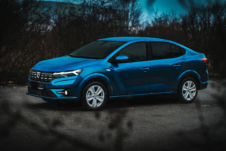 Mavi Dacia Logan sedan, otoparkta önden yan görünüm