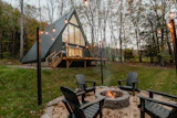 A-frame cabin lit at dusk beside a firepit and Adirondack chairs
