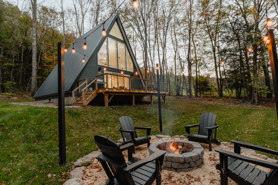 A-frame cabin lit at dusk beside a firepit and Adirondack chairs