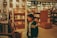 A young person in a jacket stands inside a bookstore, looking at a display featuring Marvel comics. The store has numerous shelves filled with books, creating a cozy and intellectual atmosphere.