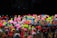 A diverse collection of colorful, small toy figurines placed closely together on sticks. The figurines are bright and varied, featuring neon shades of pink, yellow, green, blue, and orange. The background is dark, which makes the vivid colors of the toys stand out even more.