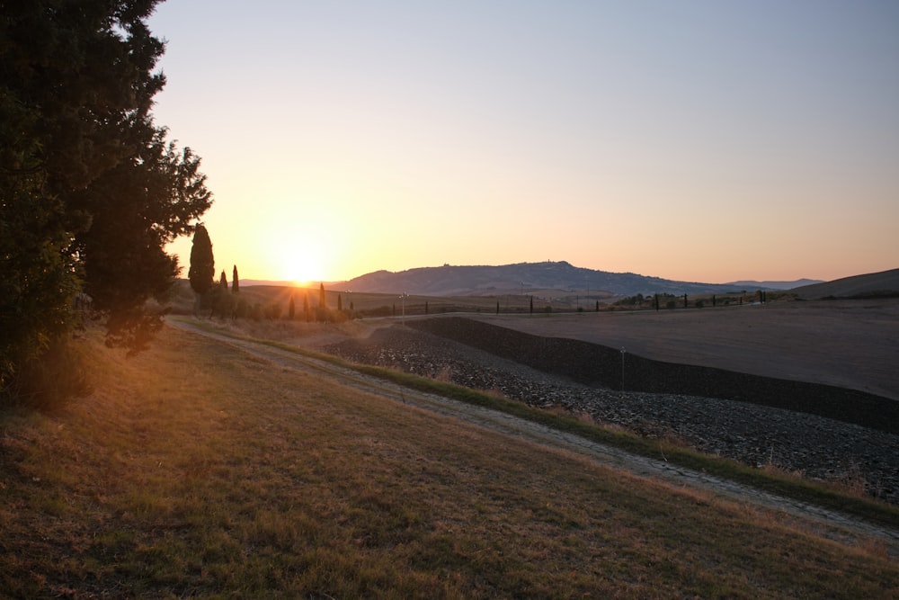 the sun is setting over a field with trees