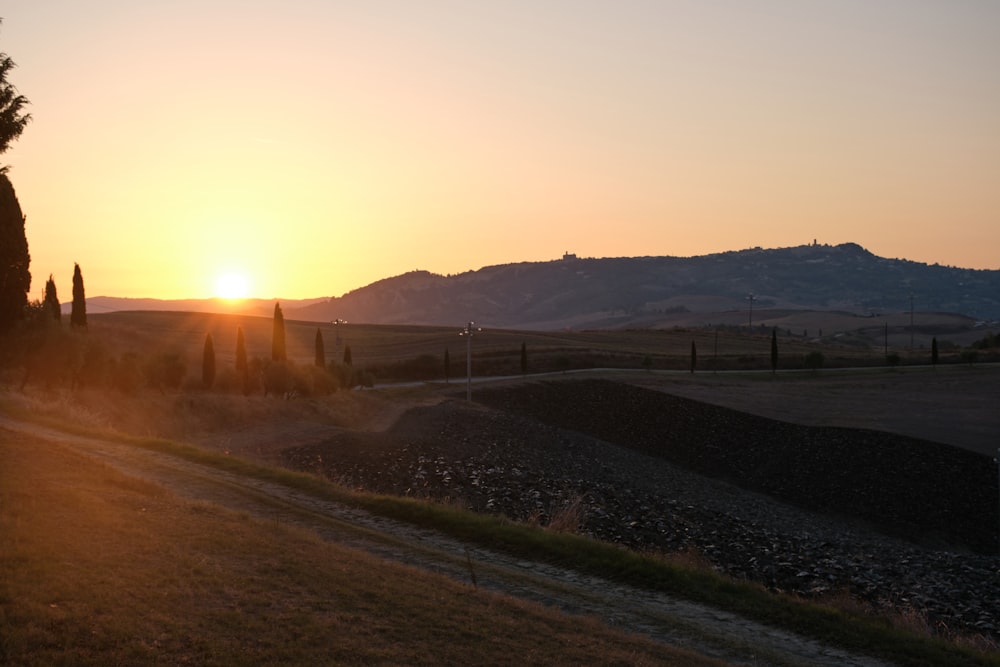 the sun is setting over a field with trees