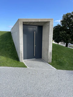 A sturdy prefabricated underground shelter partially installed in a backyard, surrounded by green grass and trees.