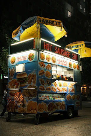 A vendor serving a Sabrett hotdog topped with mustard and onions to a smiling customer.