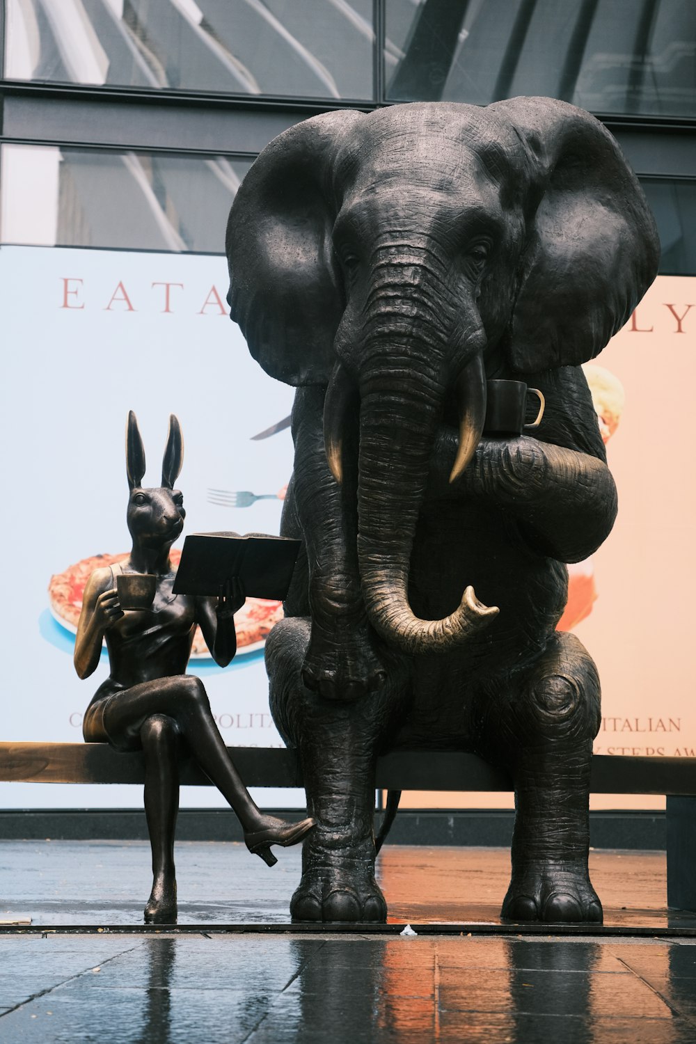 eine Statue eines Elefanten und einer Frau, die auf einer Bank sitzt