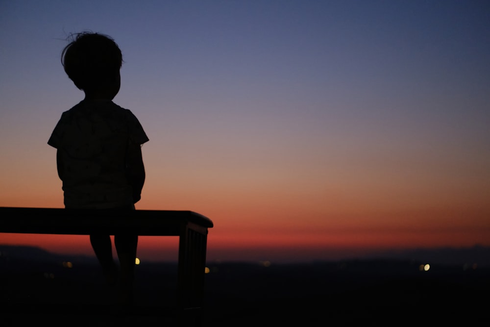 a silhouette of a child sitting on a bench