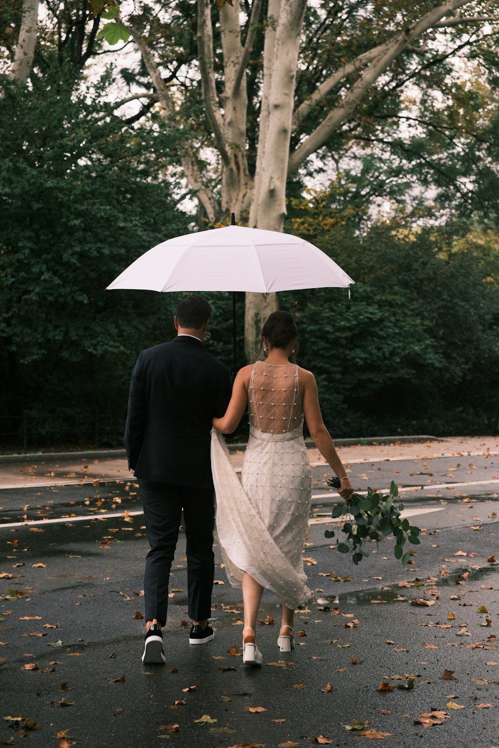 a bride and groom walking under an umbrella