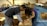 Two people are actively assembling cardboard boxes in a spacious room that appears to be set up for an event or activity. Various open and closed boxes are scattered around, and tables with items and labels can be seen in the background.