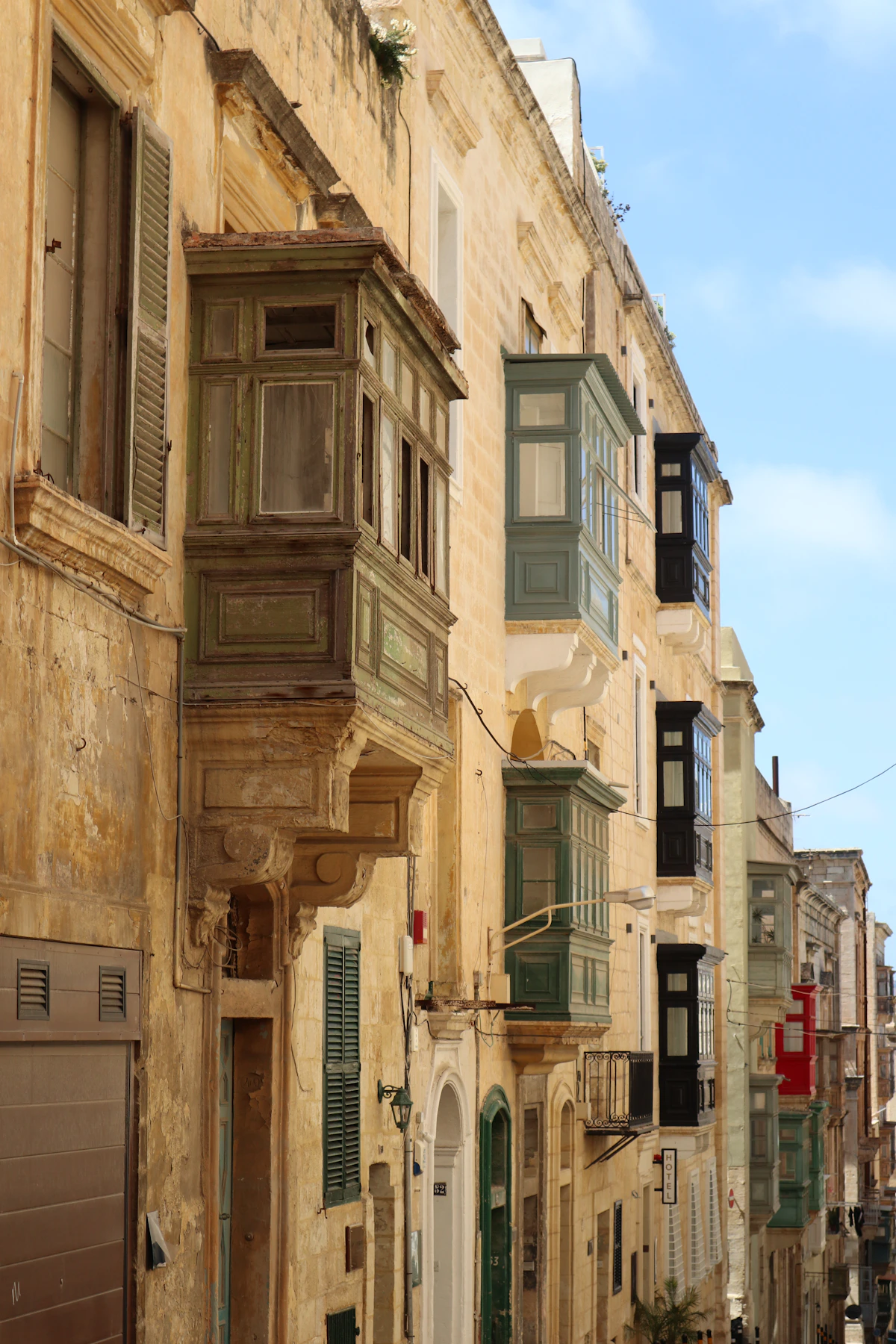Traditional green and blue timber balconies projecting from Valletta's limestone façades