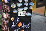 A display stand showcases colorful ceramic souvenirs, including small plates with scenic designs labeled 'Salerno' and various small, whimsical figurines like seahorses and octopuses. Signs indicate prices of €1.50 and €2.00.