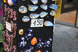 A display stand showcases colorful ceramic souvenirs, including small plates with scenic designs labeled 'Salerno' and various small, whimsical figurines like seahorses and octopuses. Signs indicate prices of €1.50 and €2.00.