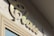 A close-up of a stylized, cursive sign that reads 'class' mounted on a textured stone wall. The sign appears to be made of a shiny, metallic material and is casting a shadow on the wall. The lighting suggests it is a sunny day.