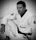 A person is wearing a martial arts gi, adorned with various patches, and is shown in a seated pose. The image features a focused, introspective expression, enhanced by the black belt around the waist. The monochrome style adds a timeless quality.
