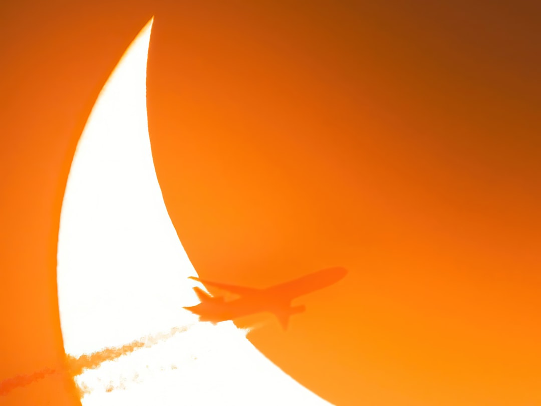 an airplane is flying in the sky at sunset, An airplane passes in front of the 2023 annular eclipse