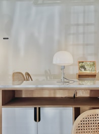 A clean, minimalist hotel room desk area with a lamp and chair.
