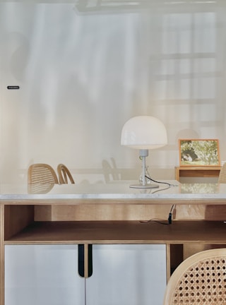 A minimalist writing desk against a white wall, featuring clean lines and a simple lamp.
