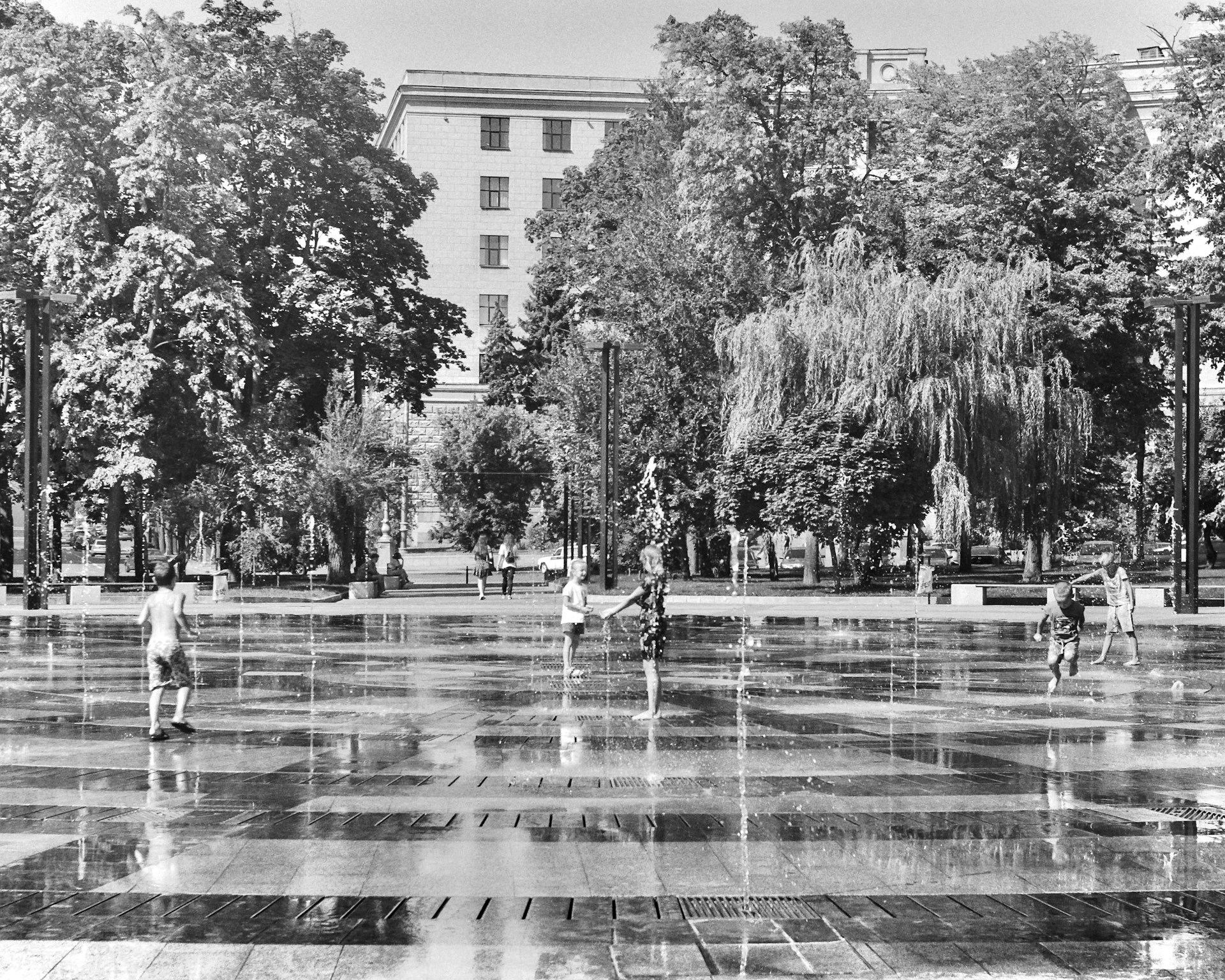 Children playing joyfully near the colorful playground surrounded by tall trees and blooming flowers.