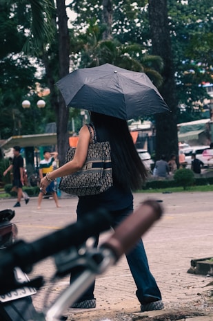 A lifestyle shot of a woman carrying a stylish, durable ladies bag while walking through a city street on a cloudy day.