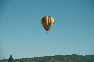 A colorful hot air balloon soaring peacefully over lush green hills at sunrise.