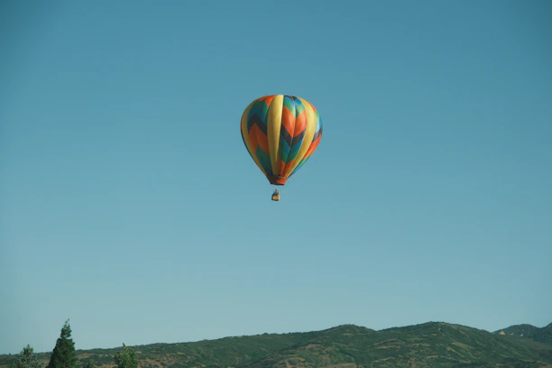 A colorful hot air balloon soaring over a scenic mountain landscape at sunrise.