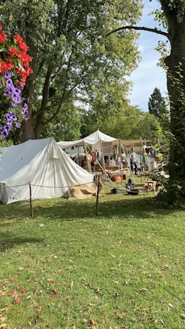 A vibrant medieval camp setup with colorful tents and people in period costumes engaging in daily activities.