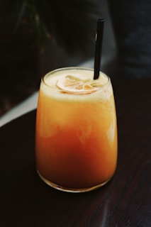 a glass of orange juice with a black straw