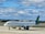 A commercial airplane from Aer Lingus is taxiing on a runway at an airport under a partly cloudy sky. The plane features a white fuselage with green and blue accents, including a green shamrock logo on the tail.