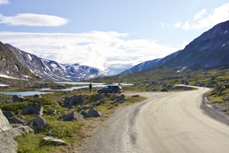 A scenic road winding through mountains with a parked rental car nearby.