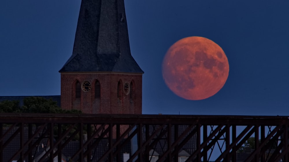 a full moon is seen behind a church steeple