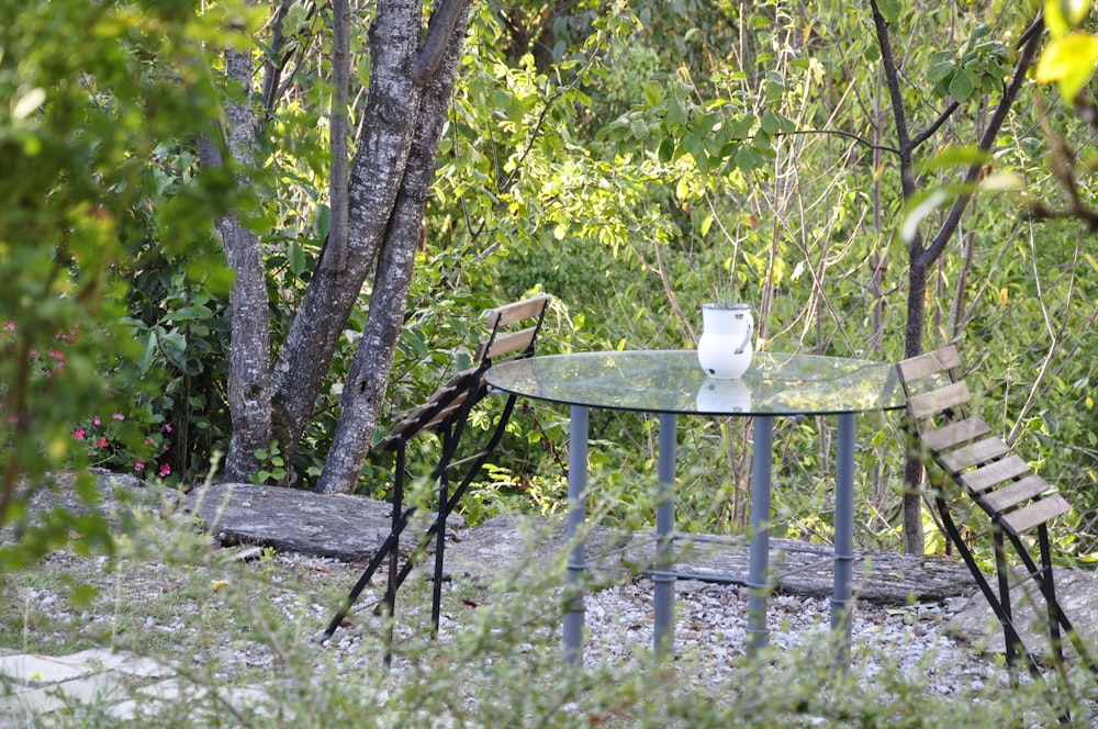 a glass table and two chairs in the woods
