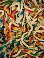 A vibrant background filled with colorful gummy worms twisting playfully around each other.
