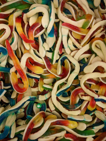 A vibrant background filled with colorful gummy worms twisting playfully around each other.