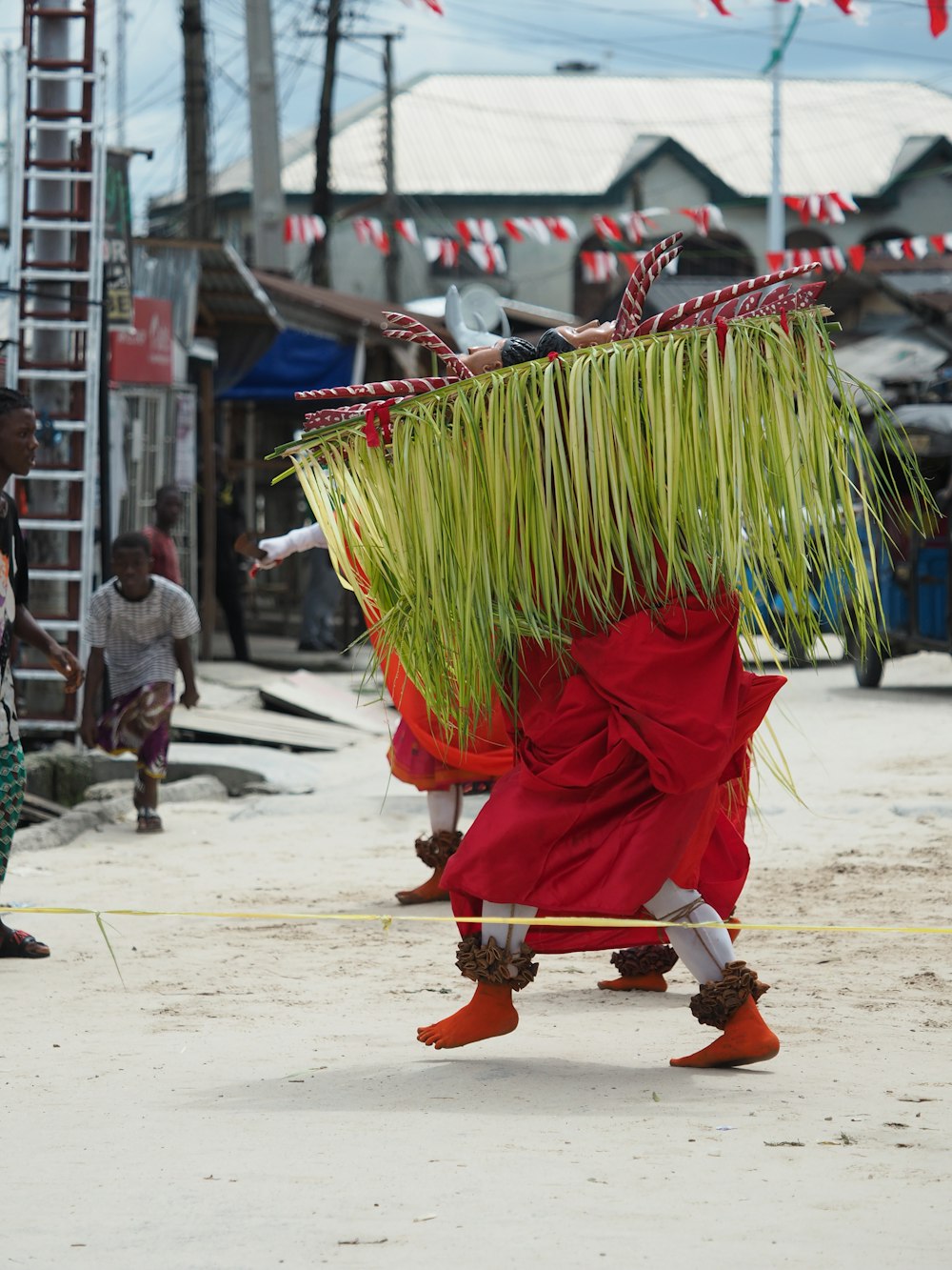 a man walking down a street carrying a bunch of grass on his back