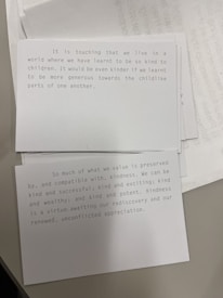 Two cards are placed on a surface, each containing printed text. The top card discusses kindness in a world where we've learned to be kind to children and emphasizes being more generous towards the childlike parts of us. The second card focuses on the value of kindness and its compatibility with success, wealth, and excitement, advocating for its rediscovery and appreciation.