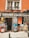 A shop front featuring various artworks displayed outside. The signage reads 'CUADROS GUAPOS.com,' with a variety of colorful illustrations and paintings showcasing cityscapes, stylized portraits, and a large paint palette. The shop is housed in an orange building with potted plants on the balcony.