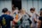 A group of people stands closely together in front of a doorway. Some have their hands on each other's shoulders, showing a sense of support or prayer. They carry backpacks, suggesting they are on a trip or mission.