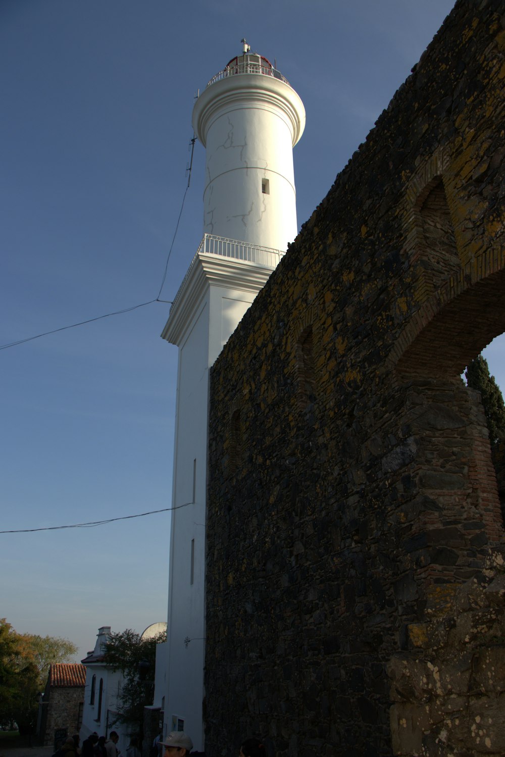 um farol branco sentado em cima de uma parede de pedra